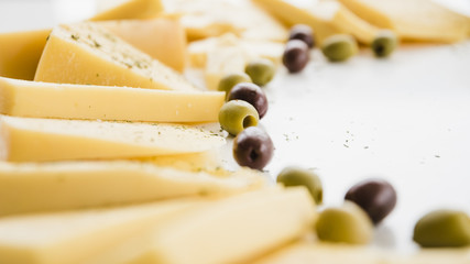 Different type of cheese slices with olives on white backdrop