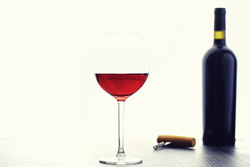 A glass of red dry wine on the table. Dark bottle and glass of wine.