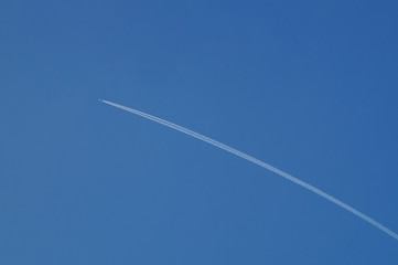 A jet plane is flying in a clear blue sky, leaving behind a white smoke plume.
