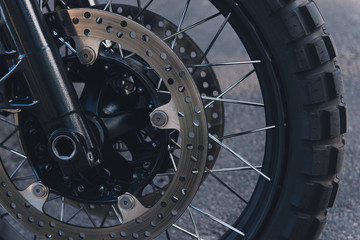 Part of a motorcycle wheel in tyre on the street. Big brake rotor and rim spokes.