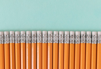 Border of orange pencils with erasers, on a blue green background with copy space