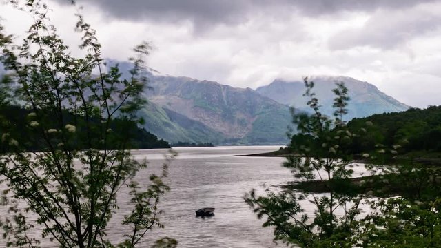 Cinematic timelapse of a boat on a scottish lake with clouds and misty scottish highlands in background