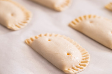 Close up of empanada, small spanish pies on baked paper. Cooking process background.