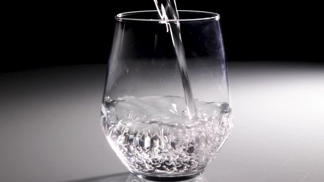 Water being poured into a clear glass with a dark background.