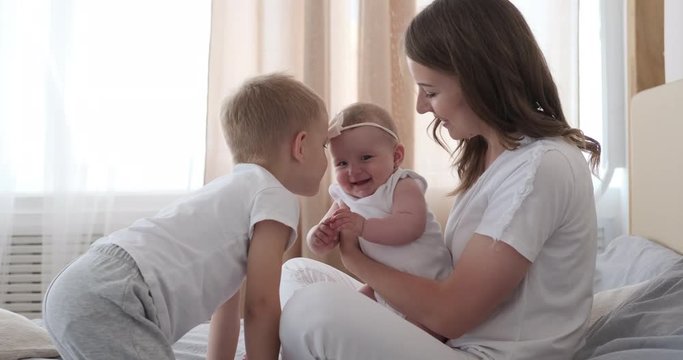 Happy mother and elder son playing with cute baby girl on bed