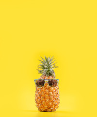 Creative pineapple looking up with sunglasses and shell isolated on yellow background, summer vacation beach idea design pattern, copy space close up