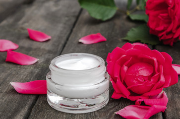 Obraz na płótnie Canvas Natural flower cosmetics with red pink flowers for face and body care in a glass jar on a wooden rustic background