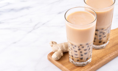 Popular Taiwan drink - Bubble milk tea with tapioca pearl ball in drinking glass on marble white table wooden tray background, close up, copy space