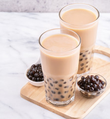 Popular Taiwan drink - Bubble milk tea with tapioca pearl ball in drinking glass on marble white table wooden tray background, close up, copy space