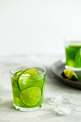 Homemade trendy iced matcha green tea or lemonade with cucumber and lime in a glass on light gray background.Healthy cold vegan beverage for hot summer day.Super food drink.Vertical orientation