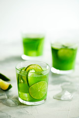 Homemade trendy iced matcha green tea or lemonade with cucumber and lime in a glass on light gray background with copy space for text.Healthy cold vegan beverage for hot summer day.Super food drink