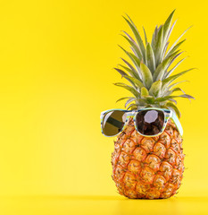 Creative pineapple looking up with sunglasses and shell isolated on yellow background, summer...