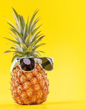 Naklejki Creative pineapple looking up with sunglasses and shell isolated on yellow background, summer vacation beach idea design pattern, copy space close up