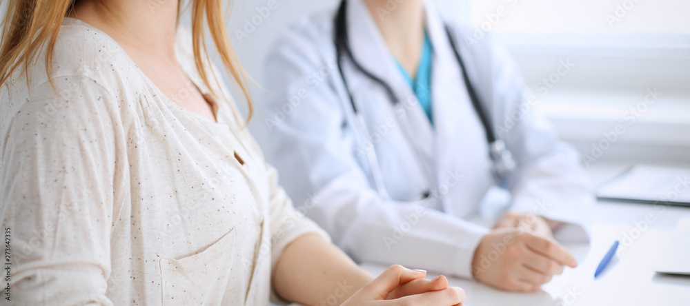 Wall mural Doctor and patient discussing something while sitting at the desk at hospital, close-up. Medicine and health care