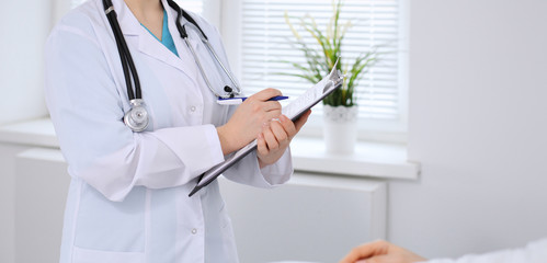 Female doctor filling up application form in hospital ward. Patient lying at the bed and listening physician. Medicine and health care