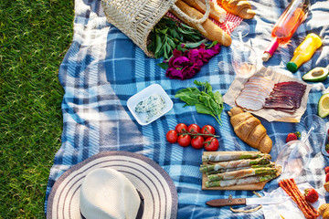 Picnic setting on the grass with basket, croissants, fruit, strawberry, asparagus and wine