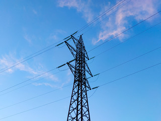 Supports high-voltage power lines against the blue sky with clouds. Electrical industry.