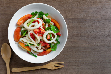 top view of spicy squid ring salad in a ceramic plate on wooden table. homemade style food concept.