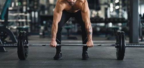 Fototapeta na wymiar Muscular guy lifting heavy barbell from gym floor