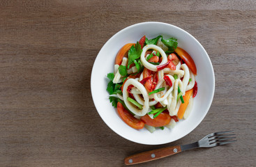 top view of spicy squid ring salad in a ceramic plate on wooden table. homemade style food concept.