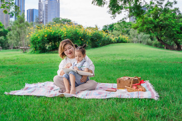 Asian grandmother and granddaughter sitting on the green glass field outdoor, Asian family enjoying picnic together in summer day