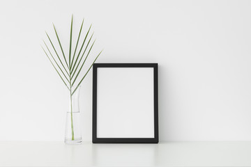 Black frame mockup with palm leaf in a glass vase. Portrait orientation.