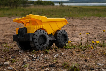 Obraz premium A child's yellow dump truck abandoned on the ground by a lake, side on view