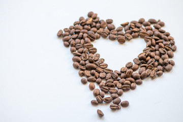 Ein Haufen geröstete Kaffeebohnen mit einem Loch in Herzform auf weißem Hintergrund lädt zum Kaffeegenuss ein