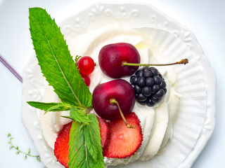 Pavlova meringue cake with fresh berries, mint on white plate with fork