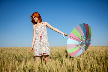 Girl with umbrella on wheat field with blue sky on background