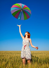 Girl with umbrella on wheat field with blue sky on background