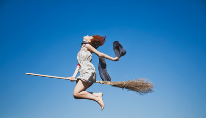 Young redhead witch on broom flying in the sky