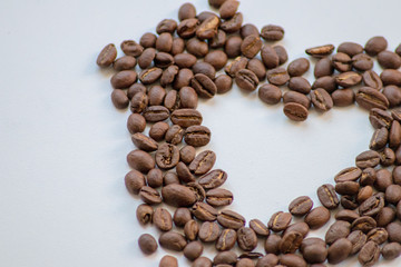 Ein Haufen geröstete Kaffeebohnen mit einem Loch in Herzform auf weißem Hintergrund lädt zum Kaffeegenuss ein