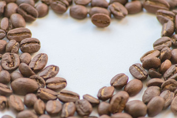 Ein Haufen geröstete Kaffeebohnen mit einem Loch in Herzform auf weißem Hintergrund lädt zum Kaffeegenuss ein