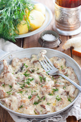Forest mushrooms in sour cream sauce on a frying pan on a wooden table, selective focus