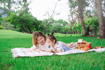 Asian grandmother and granddaughter laying on the green glass field outdoor, family enjoying picnic together in summer day