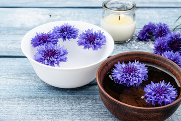 blue cornflowers lie in the water in a bowl near a burning candle on the background of the old blue boards.