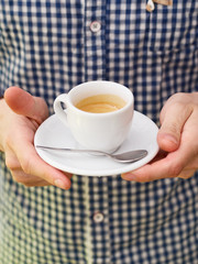Close up of barista man hands serving freshly brewed cappucino coffee while standing in coffee shop. Focus on male hands holding a big white ceramic cup of coffee with copyspace