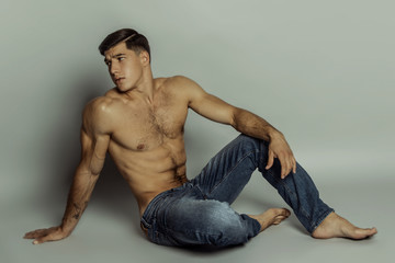 Muscle strong beautiful stripped male model in denim blue jeans on grey isolated font background
