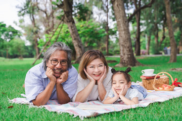 Asian grandparents and granddaughter are lying on the grass field outdoor, asian family concept