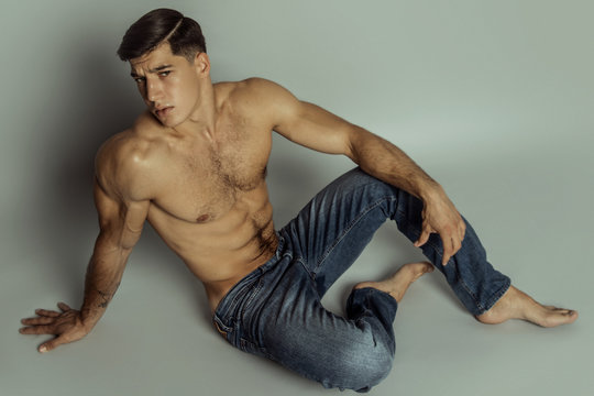 Muscle strong beautiful stripped male model in denim blue jeans on grey isolated font background
