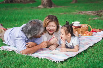 Fototapeta premium Asian grandparents and granddaughter are lying on the grass field outdoor, asian family concept