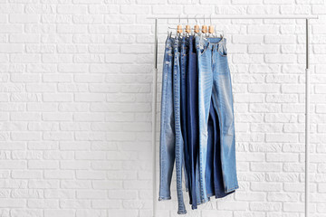 Clothes rack with different stylish jeans pants on white brick background