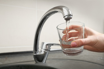 Woman filling glass with water from kitchen faucet