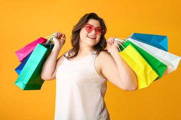 Happy plus size woman with shopping bags on color background