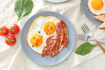 Plate with tasty fried eggs and bacon on table