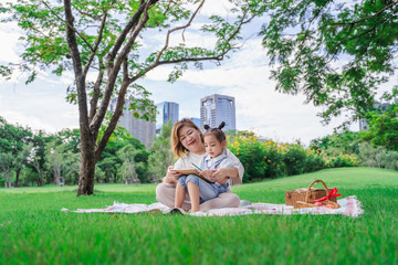 Asian grandmother and granddaughter sitting on the green glass field outdoor, Asian family enjoying picnic together in summer day