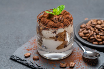 Classic tiramisu dessert in a glass on stone serving board on dark concrete background