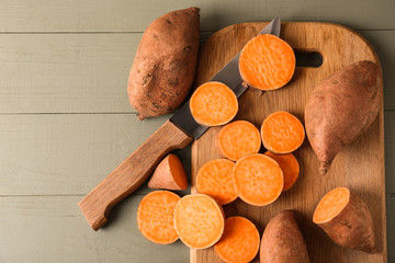 Cutting board and knife with raw sweet potato on wooden background