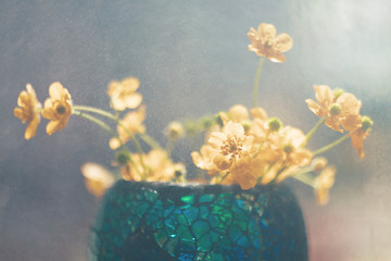Yellow small buttercups in a stylish blue vase in oriental style stand on the window. Drops of water hover in the air. Cozy cute still life. The concept of summer flowering, interior decoration.
